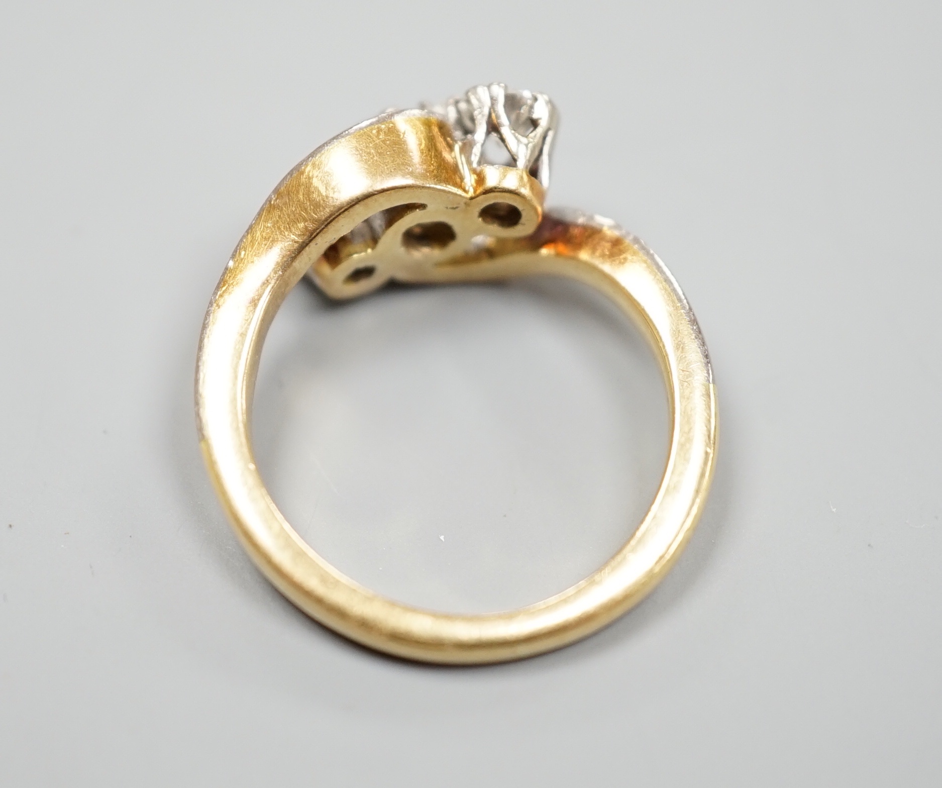 A yellow metal and three stone diamond set crossover ring, with diamond set shoulders, size I, gross 4.6 grams.